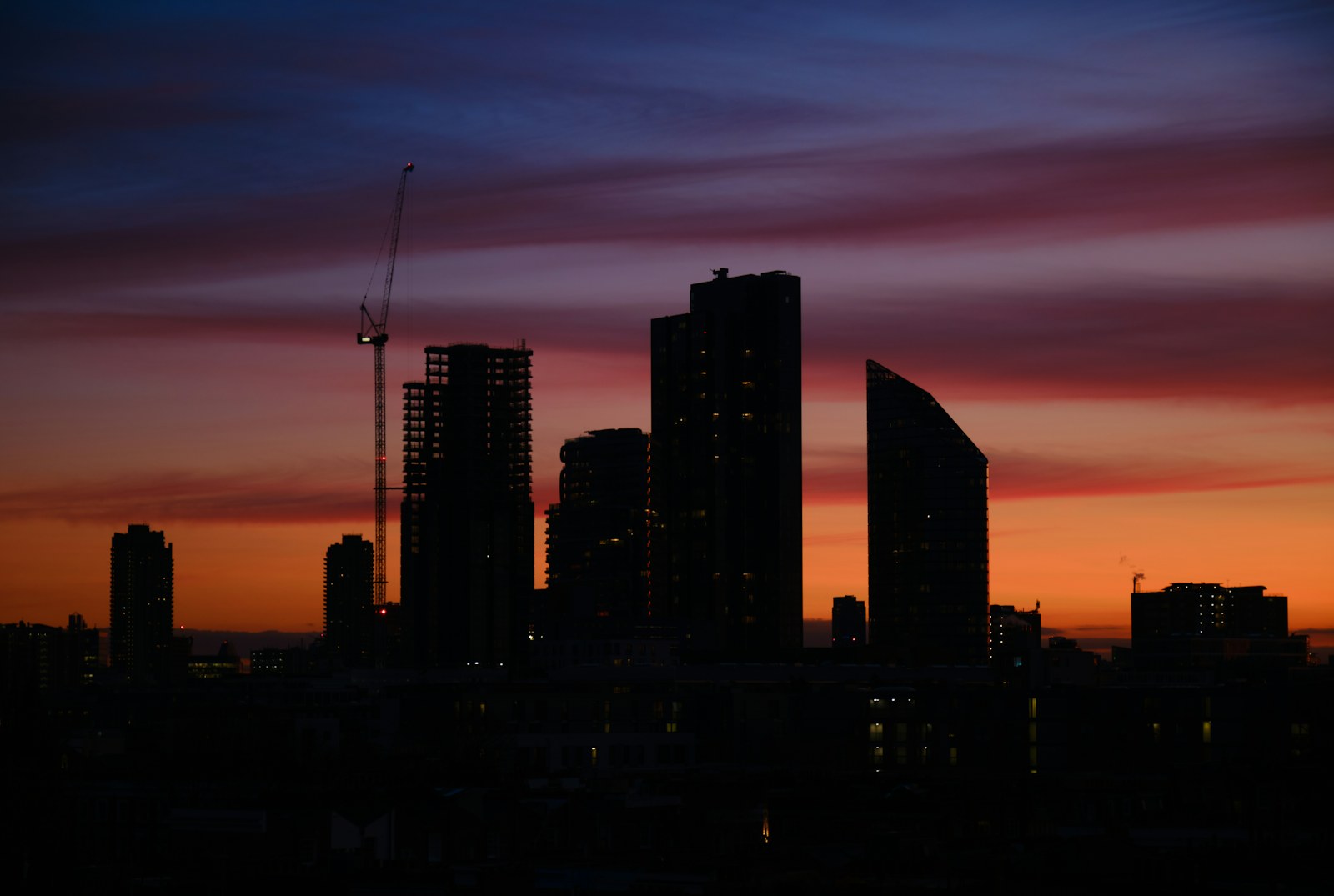 London towers and construction cranes silhouetted against an orange and purple sunset.