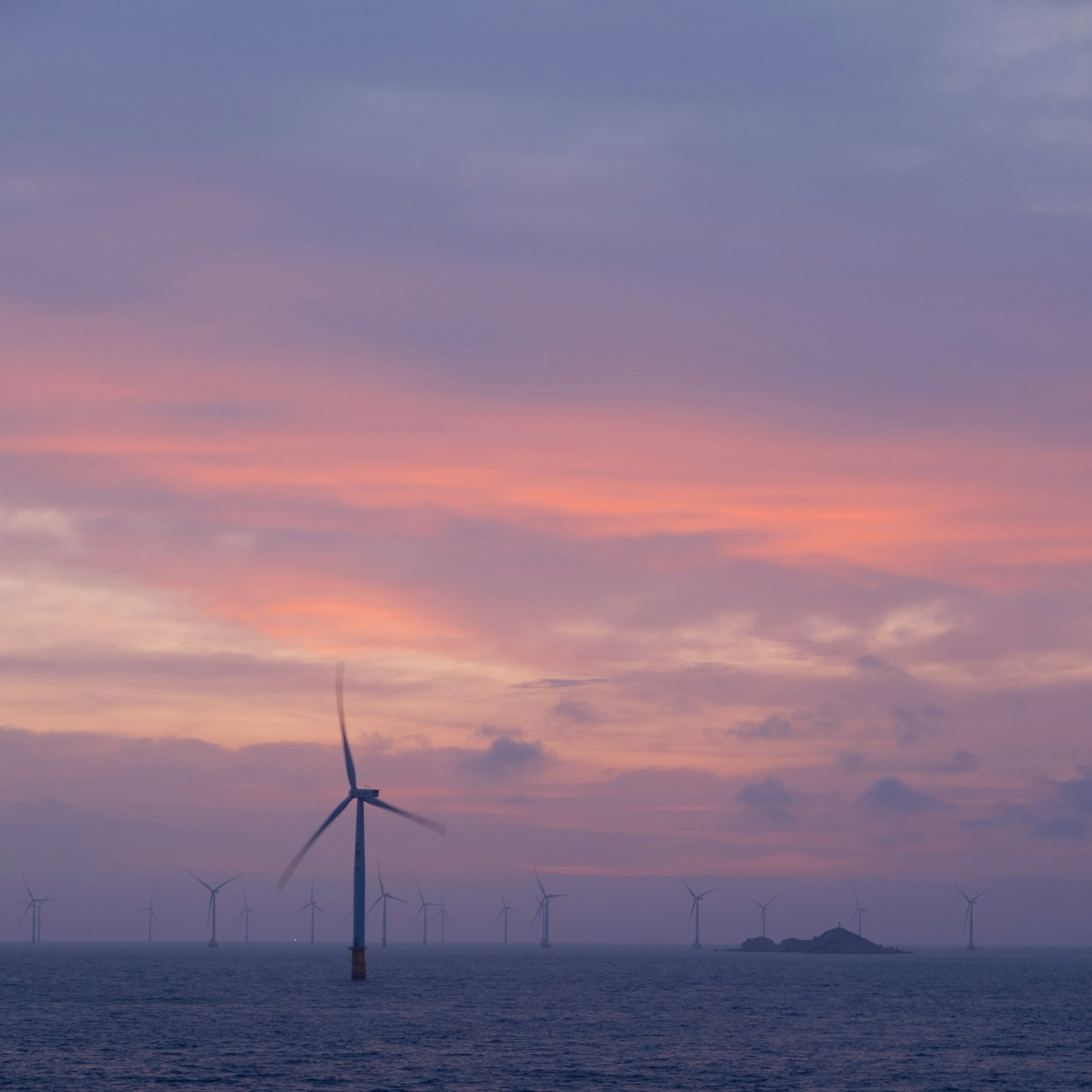 Offshore wind turbines beneath a pink and purple sunset sky.